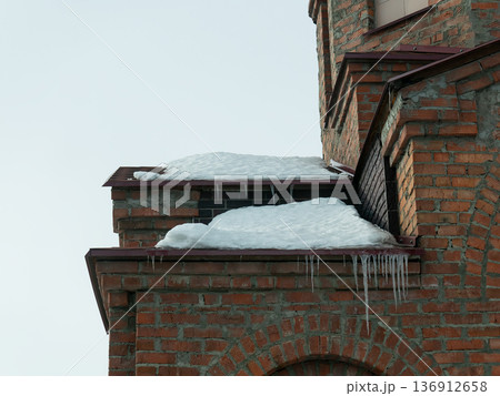 Melting snow and icicles hanging down from a brick building cornice. Winter weather and seasonal architectural detail. 136912658