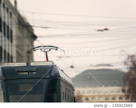 Rear view of a modern tram trolley pole, also known as a pantograph, against a blurred city background. Urban public transport for modern travel. Rear view of a modern tram trolley pole, also known as a pantograph, against a blurred city background. Urban public transport for modern travel. 136912664