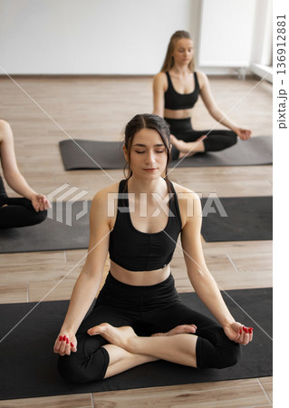 Three women in black activewear practice meditation and mindfulness on yoga mats in a bright studio room 136912881