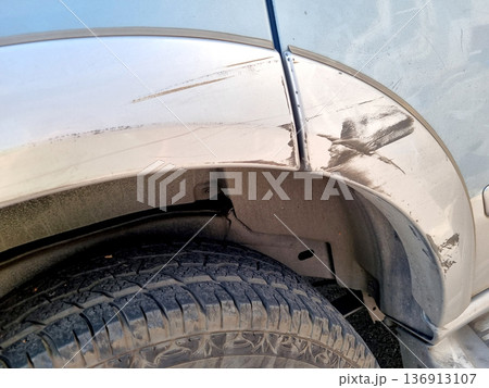 Close-up of deep scratches and black scuff marks on a silver car fender and wheel arch. Vehicle body damage from a minor collision or scraping against a wall. Professional automotive repair concept. 136913107