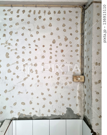 Rough concrete wall prepared for ceramic tiling with notched adhesive spots and exposed electrical wiring and old socket. Home renovation, construction phase and interior remodeling scene. Rough concrete wall prepared for ceramic tiling with notched adhesive spots and exposed electrical wiring and old socket. Home renovation, construction phase and interior remodeling scene. 136913110