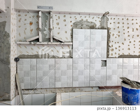 Kitchen wall renovation with grey ceramic tiles being installed over concrete. Professional home improvement process showing construction details, adhesive marks and tile placement on site. Kitchen wall renovation with grey ceramic tiles being installed over concrete. Professional home improvement process showing construction details, adhesive marks and tile placement on site. 136913113