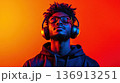 Young man enjoying music with headphones against a vibrant orange and yellow background, showcasing a moment of relaxation and connection with sound 136913251