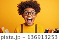 Excited child with curly hair and glasses holding books in front of a bright yellow background celebrating learning and reading 136913253