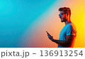 Young man interacting with smartphone in vibrant atmospheric lighting during the evening 136913254