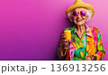 Elderly woman enjoys a tropical drink wearing colorful attire against a vibrant pink background during a sunny day outing 136913256