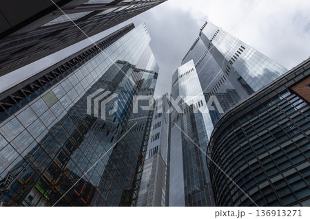 Modern glass skyscrapers reaching towards a cloudy sky 136913271