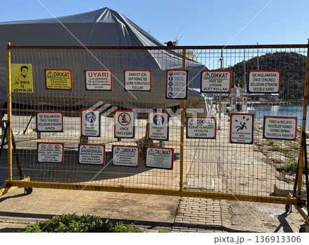 Warning safety signs on a metal gate in an outdoor area on a sunny day 136913306