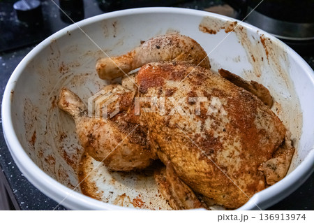 Raw whole chicken seasoned with spices in a white bowl, ready for cooking. Preparation for a delicious meal, cooking at home concept. 136913974
