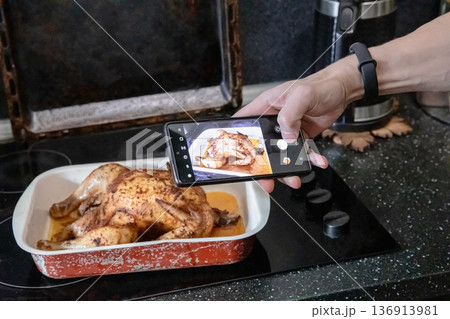 Man taking photo of a whole roasted chicken in a baking dish with smartphone. Social media food blogging concept. Man taking photo of a whole roasted chicken in a baking dish with smartphone. Social media food blogging concept. 136913981