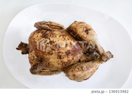 Whole roasted chicken on a white plate, prepared for a meal. Delicious cooked poultry dish for dinner or holiday food concept. Whole roasted chicken on a white plate, prepared for a meal. Delicious cooked poultry dish for dinner or holiday food concept. 136913982