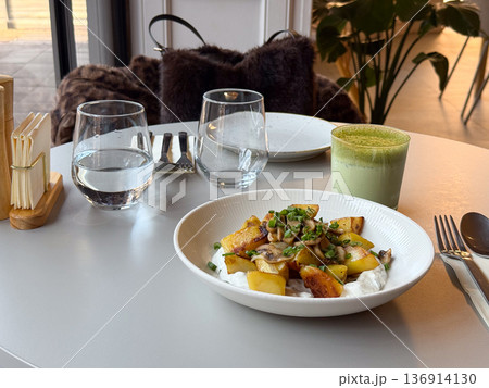 Roasted potato dish with mushroom and green latte on table. Modern cafe dining, healthy choice, balanced meal, and urban lifestyle concept Roasted potato dish with mushroom and green latte on table. Modern cafe dining, healthy choice, balanced meal, and urban lifestyle concept 136914130