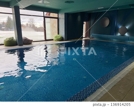 Indoor swimming pool with panoramic window and calm blue water in spa. Recreation facility, fitness activity, leisure tourism, and healthy lifestyle environment Indoor swimming pool with panoramic window and calm blue water in spa. Recreation facility, fitness activity, leisure tourism, and healthy lifestyle environment 136914205