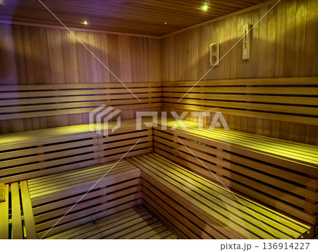 Wooden sauna interior with tiered benches and warm ambient lighting. Heat therapy, detox ritual and traditional wellness practice Wooden sauna interior with tiered benches and warm ambient lighting. Heat therapy, detox ritual and traditional wellness practice 136914227