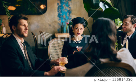 Stylish couple in vintage attire enjoying drinks at intimate retro table 136914350