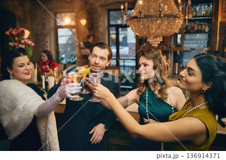 Elegant group clinking cocktails in vintage bar under crystal chandelier. 136914371