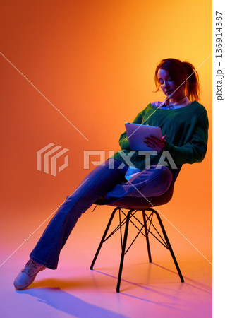 Young woman using tablet for digital work in studio with colorful background. 136914387