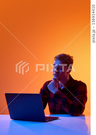 Young professional analyzing data on laptop against gradient background. 136914410