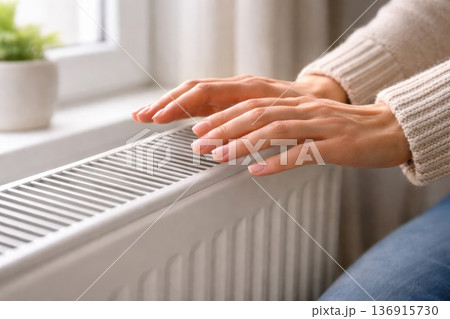 Female hands warming over home radiator heater during cold winter day indoors Female hands warming over home radiator heater during cold winter day indoors 136915730