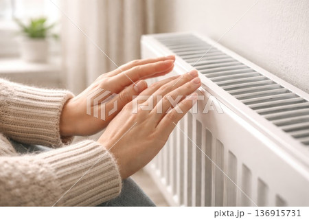 Close up of hands feeling warmth from modern radiator heating system in home interior 136915731