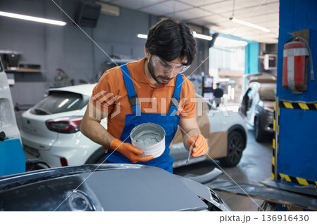 Technician is meticulously prepping a car panel with primer in a garage workshop Technician is meticulously prepping a car panel with primer in a garage workshop 136916430