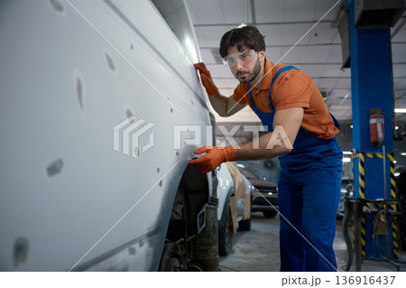An auto body technician is meticulously inspecting a car panel in the repair shop today An auto body technician is meticulously inspecting a car panel in the repair shop today 136916437
