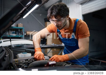 A mechanic checks engine oil with gloves in a garage A mechanic checks engine oil with gloves in a garage 136916439