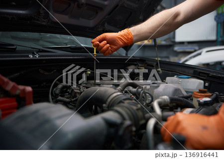 A mechanic checks engine oil with gloves in a garage A mechanic checks engine oil with gloves in a garage 136916441