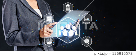 A professional businesswoman uses a digital tablet featuring glowing holographic icons for human resources, team management, data analytics, and global networking on a dark background A professional businesswoman uses a digital tablet featuring glowing holographic icons for human resources, team management, data analytics, and global networking on a dark background 136916572