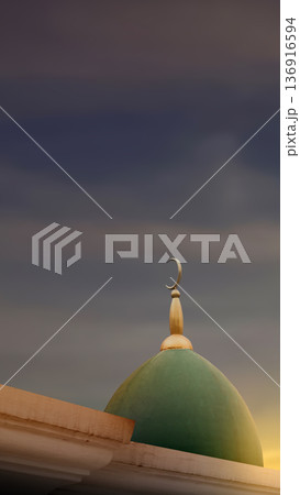 Close-up of a green mosque dome and golden crescent finial against a dramatic dark cloudy sky at sunset. Symbolic of Islamic faith, prayer, and spiritual peace Close-up of a green mosque dome and golden crescent finial against a dramatic dark cloudy sky at sunset. Symbolic of Islamic faith, prayer, and spiritual peace 136916594