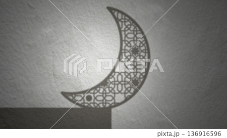 Minimalist shadow of an intricate Islamic patterned crescent moon cast on a light grey textured wall, perfect for Ramadan, Eid al-Fitr, and Eid al-Adha greeting cards and backgrounds 136916596