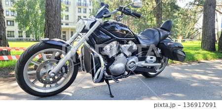 Black powerful touring motorcycle parked on asphalt road near green trees. Cruiser for travel or road trip display. Transportation vehicle. 136917091