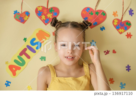 Tears of joy in the eyes of a child with autism spectrum disorder. A girl on a background decorated with puzzle pieces and hearts as a sign of support and caring for special children 136917110