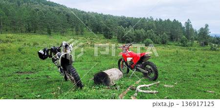 Two dirt bikes parked on a green grassy hill with a forest background. Off-road exploration adventure. Freedom travel hobby. Two dirt bikes parked on a green grassy hill with a forest background. Off-road exploration adventure. Freedom travel hobby. 136917125