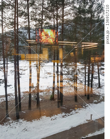 Winter pine forest with artificial fire display through window reflection. Outdoor relaxation for cold weather and cozy atmosphere. Winter pine forest with artificial fire display through window reflection. Outdoor relaxation for cold weather and cozy atmosphere. 136917210