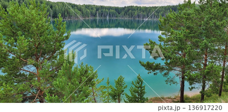 Lake with turquoise water surrounded by green forest. Summer landscape with calm water reflection. Nature beauty and environmental conservation. 136917220
