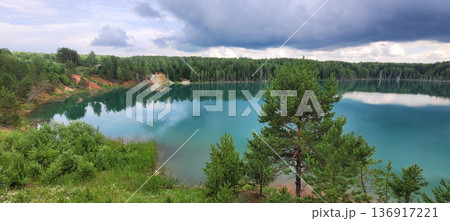 Beautiful turquoise quarry lake surrounded by green forest and cloudy sky reflecting on water. Nature landscape for travel and ecology concepts. Beautiful turquoise quarry lake surrounded by green forest and cloudy sky reflecting on water. Nature landscape for travel and ecology concepts. 136917221