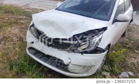 White car damaged in a front-end collision, showing dents and broken parts. Concept of road accident, car insurance claim, and vehicle repair service. White car damaged in a front-end collision, showing dents and broken parts. Concept of road accident, car insurance claim, and vehicle repair service. 136917253