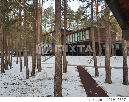Modern lodge buildings with large windows nestled amongst tall pine trees on a snowy winter day. Winter wonderland architecture, resort, vacation. 136917257