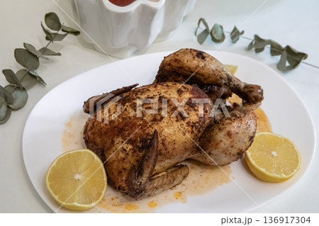 Whole roasted chicken on white plate with lemon slices. Cooked poultry for family dinner or restaurant menu display. Food photography concept. 136917304