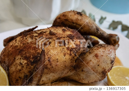 Roasted whole chicken on a plate with spices and lemon slices. Delicious homemade meal for dinner, festive occasion, or holiday celebration. 136917305