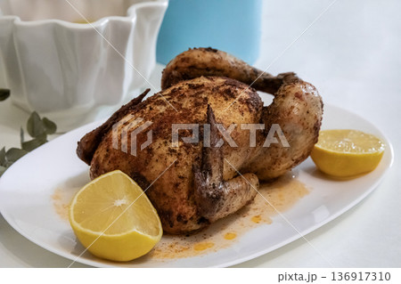 Whole roasted chicken with lemon on a white plate. Homemade cooked bird dish for dinner or holiday meal. Culinary food concept. 136917310