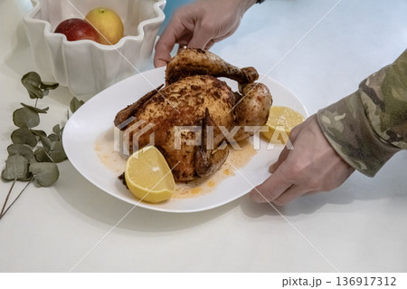 Man serving roasted chicken with lemon on white plate for dinner. Homemade cooking, healthy eating, and festive meal concept for Thanksgiving. Man serving roasted chicken with lemon on white plate for dinner. Homemade cooking, healthy eating, and festive meal concept for Thanksgiving. 136917312