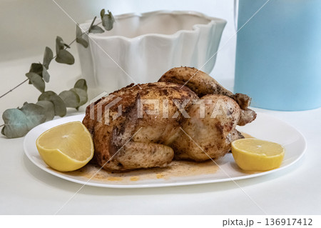 Whole roasted chicken with lemon on a white plate. Delicious baked poultry for dinner at home, served fresh and warm. 136917412