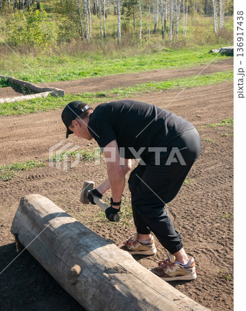 Young man drives in a log with a mallet outdoors. Fitness or outdoor physical workout concept. For health, training, lifestyle. 136917438