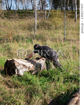 Man in black clothes pushes a heavy log in a natural environment. Strength and effort concept for outdoor work. 136917447