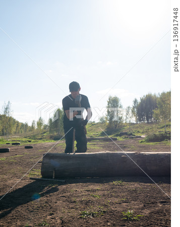 Man in black t-shirt and cap chopping wood with axe outdoors. Physical strength, power, and determination concept for fitness and work activity. Man in black t-shirt and cap chopping wood with axe outdoors. Physical strength, power, and determination concept for fitness and work activity. 136917448