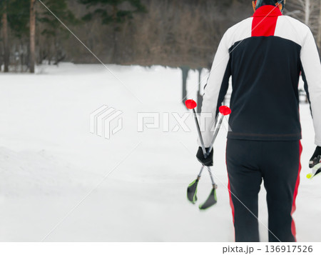 Man walking in nature with cross country skis over shoulder. Winter sports activity and healthy lifestyle background. Man walking in nature with cross country skis over shoulder. Winter sports activity and healthy lifestyle background. 136917526