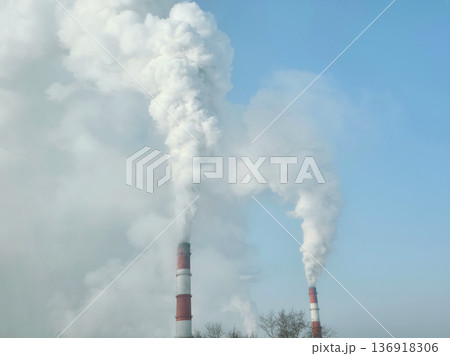 Thick white smoke plumes rising from factory chimney against clear sky. Industrial pollution and environmental emission concept. Thick white smoke plumes rising from factory chimney against clear sky. Industrial pollution and environmental emission concept. 136918306