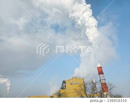 Industrial plant emitting thick white smoke from chimney into cloudy blue sky. Environmental pollution from factory smokestack concept. Industrial plant emitting thick white smoke from chimney into cloudy blue sky. Environmental pollution from factory smokestack concept. 136918310